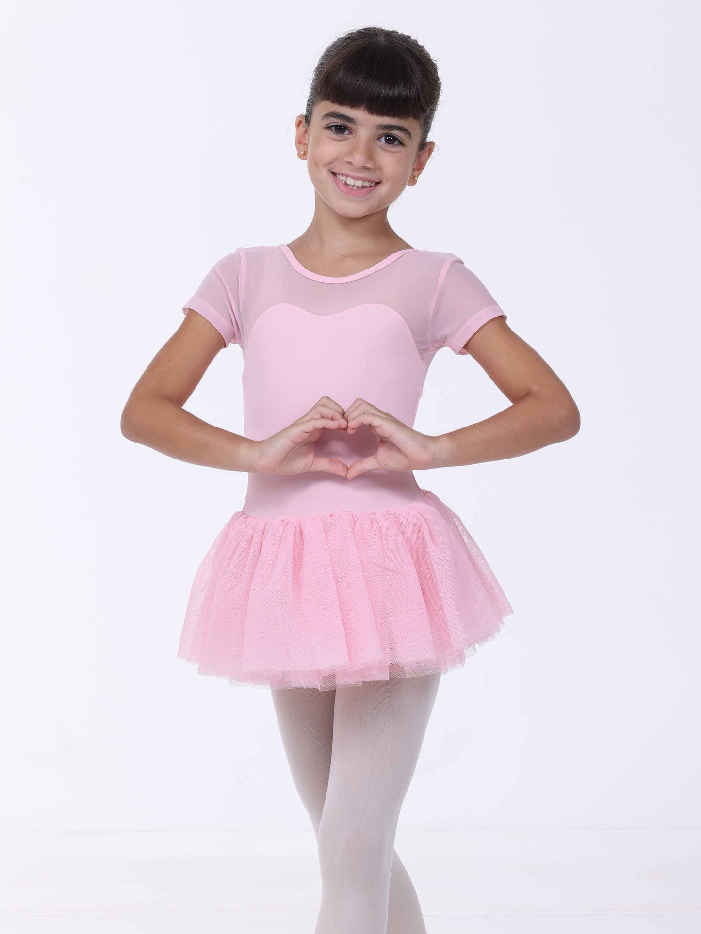 Young girl in a pink ballet outfit making a heart shape with her hands on a white background