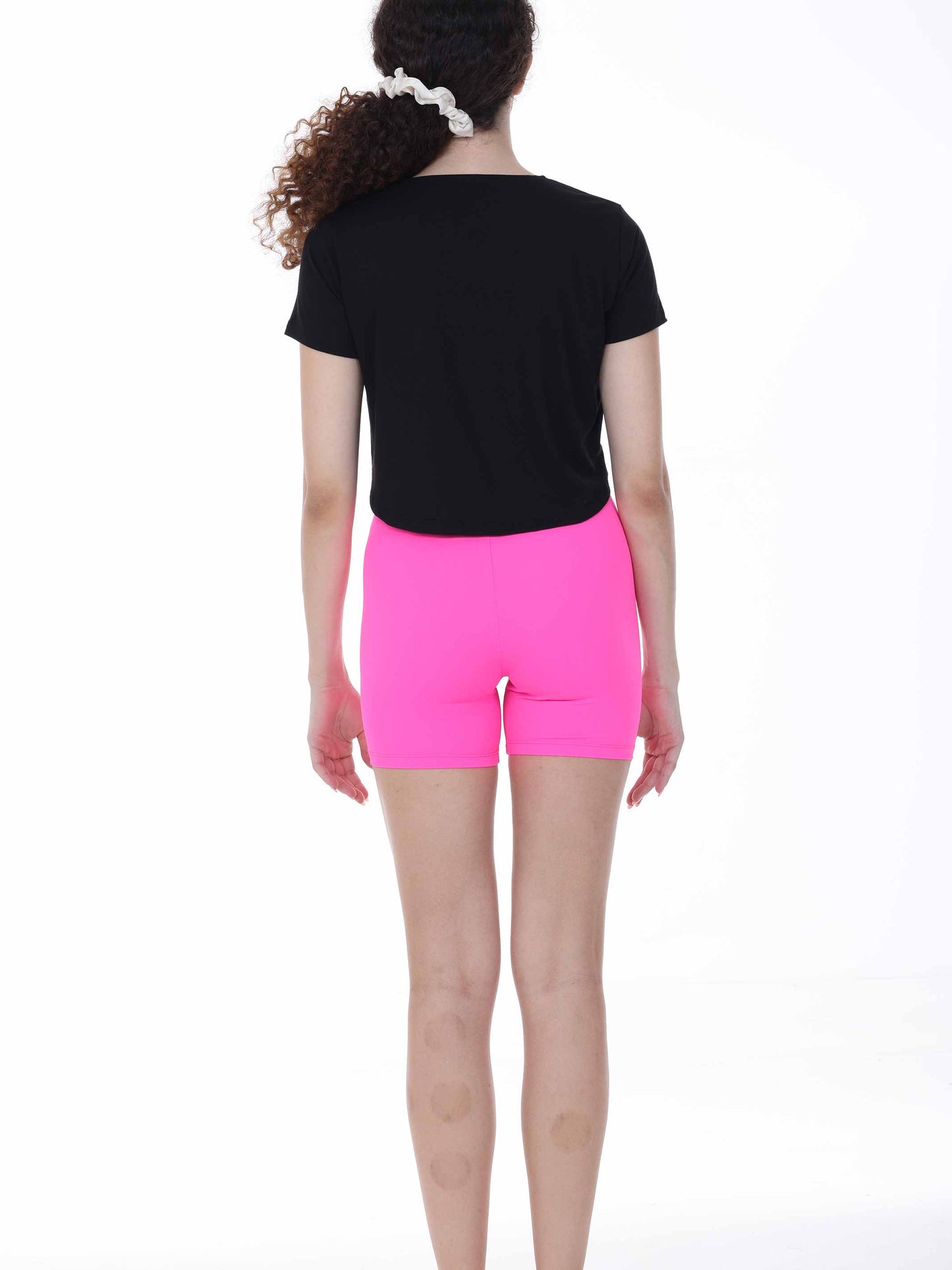 Person wearing a black t-shirt and bright pink shorts on a white background
