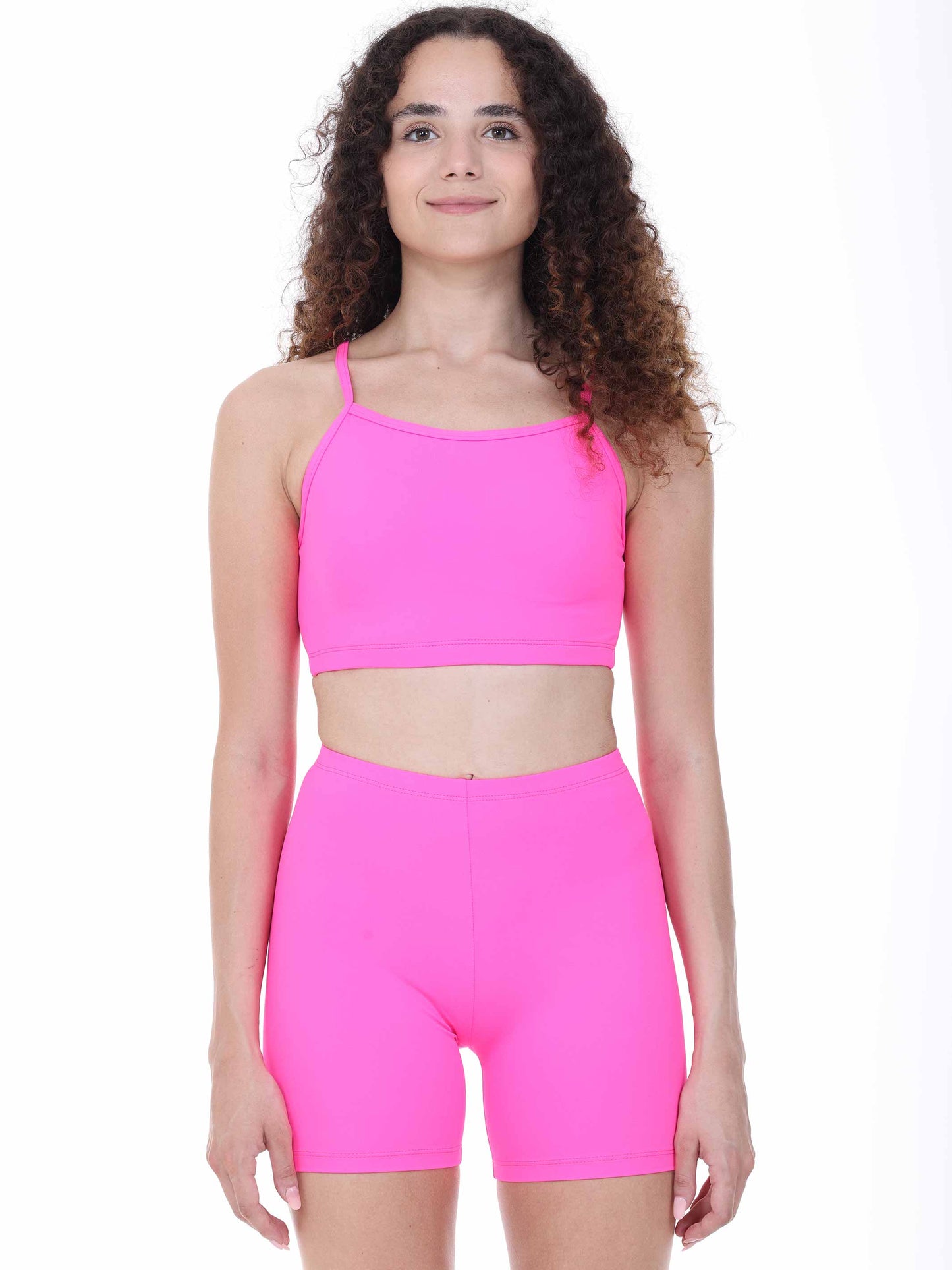 Woman wearing a bright fuchsia sports bra and shorts set on a white background