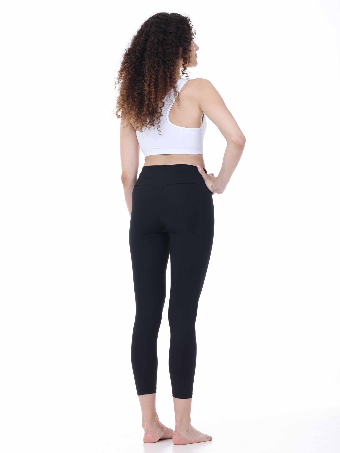 Woman wearing black leggings and a white sports bra on a white background