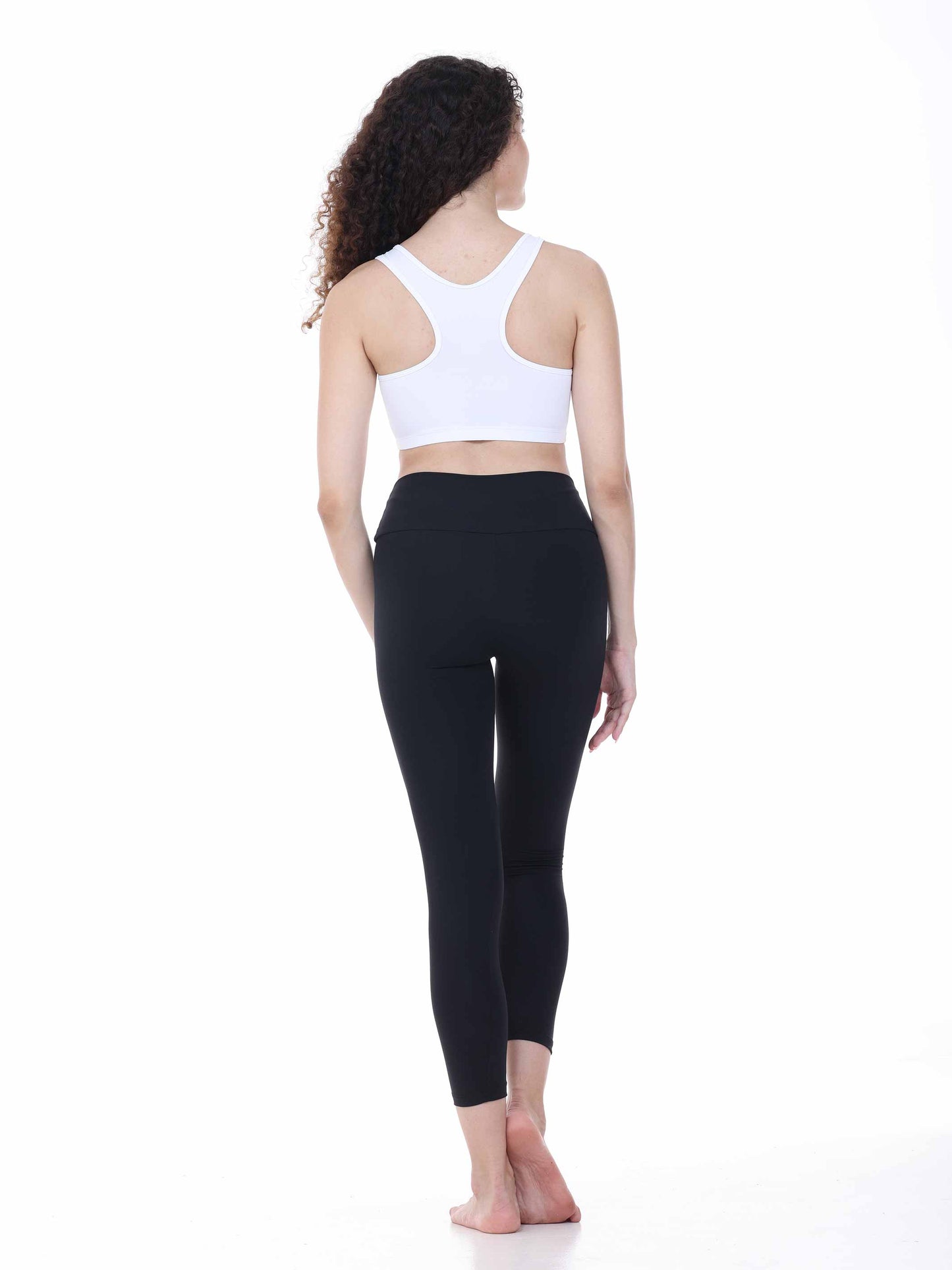 Woman wearing a white sports bra and black leggings on a white background