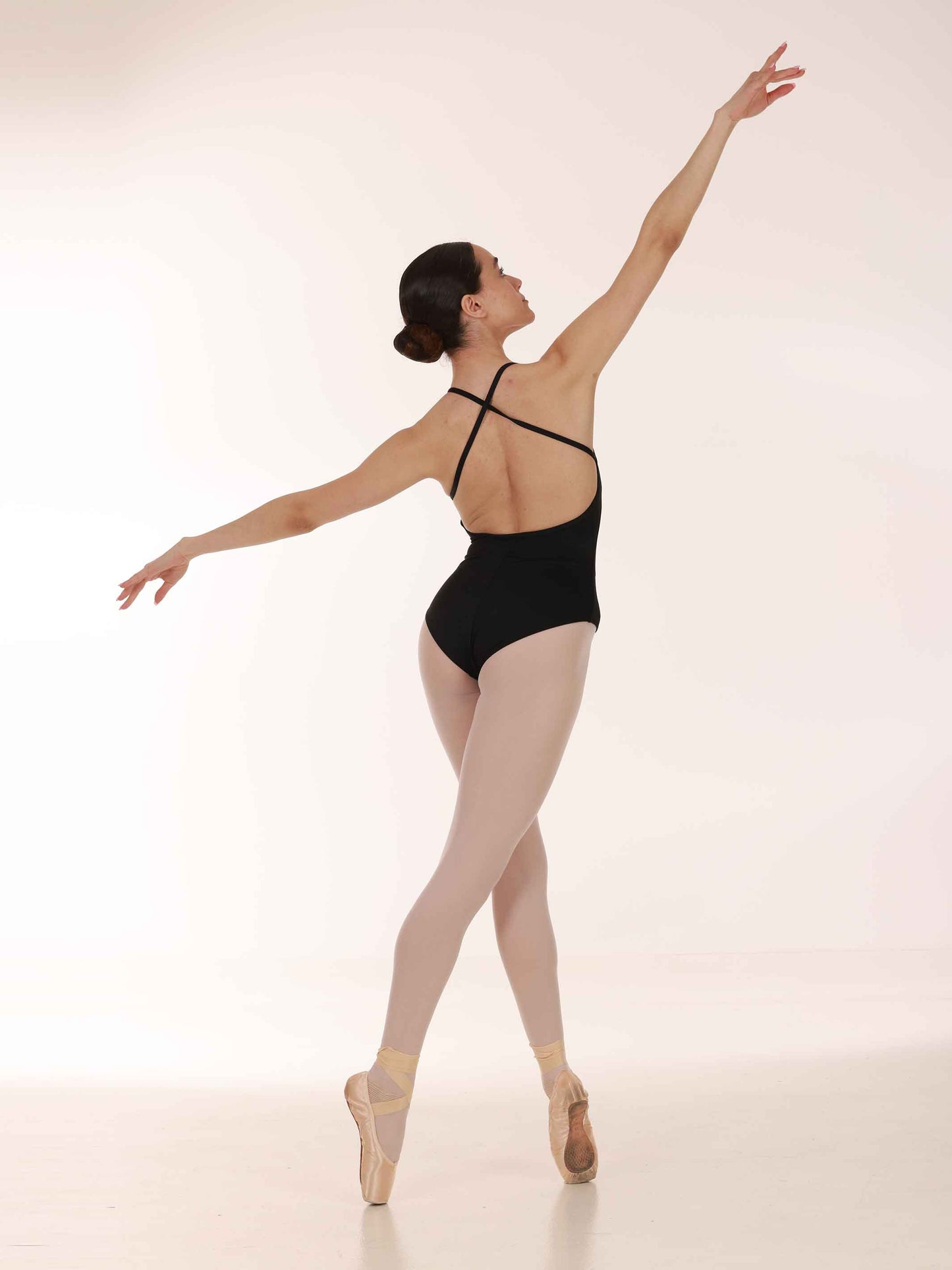 Ballerina in a black leotard and white tights posing on a white background