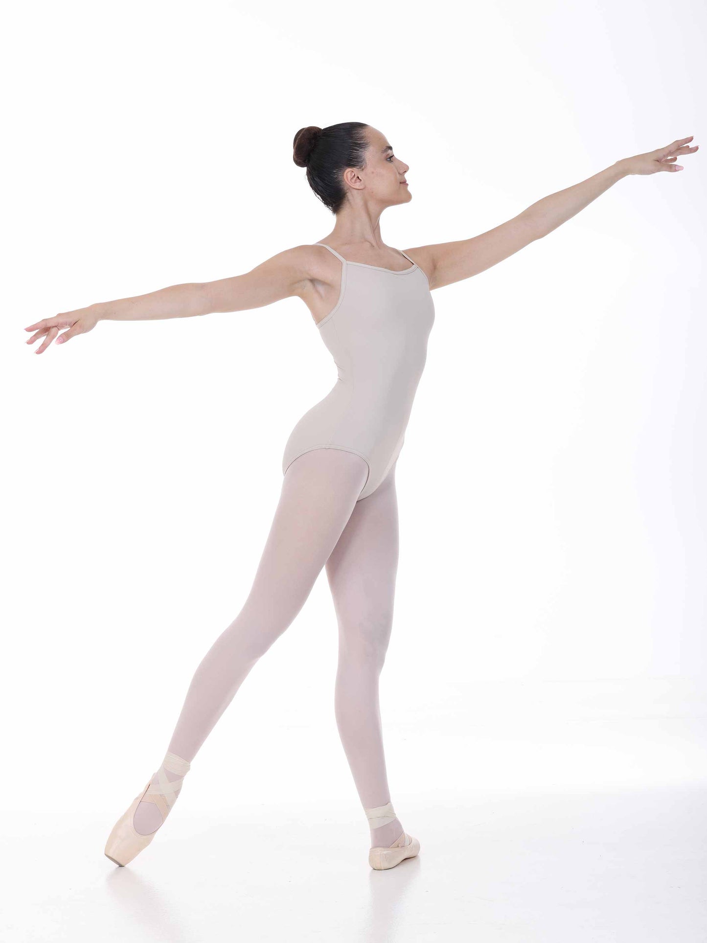 Ballerina in a nude leotard and tights posing on a white background