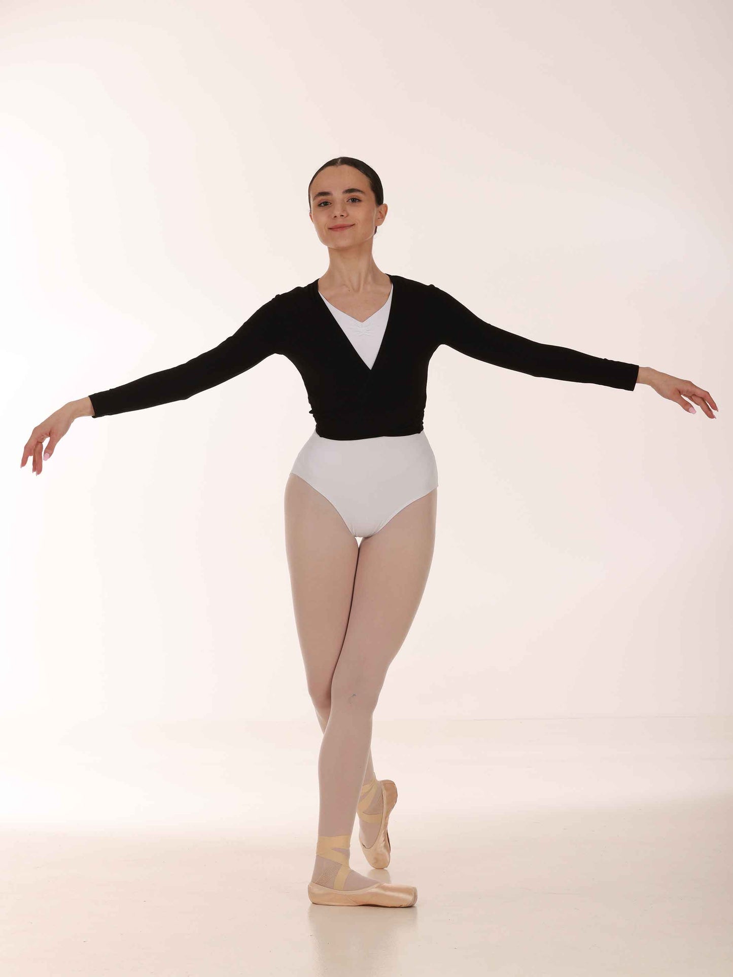 Ballerina in a black long-sleeve warmer top and white leotard posing on a white background