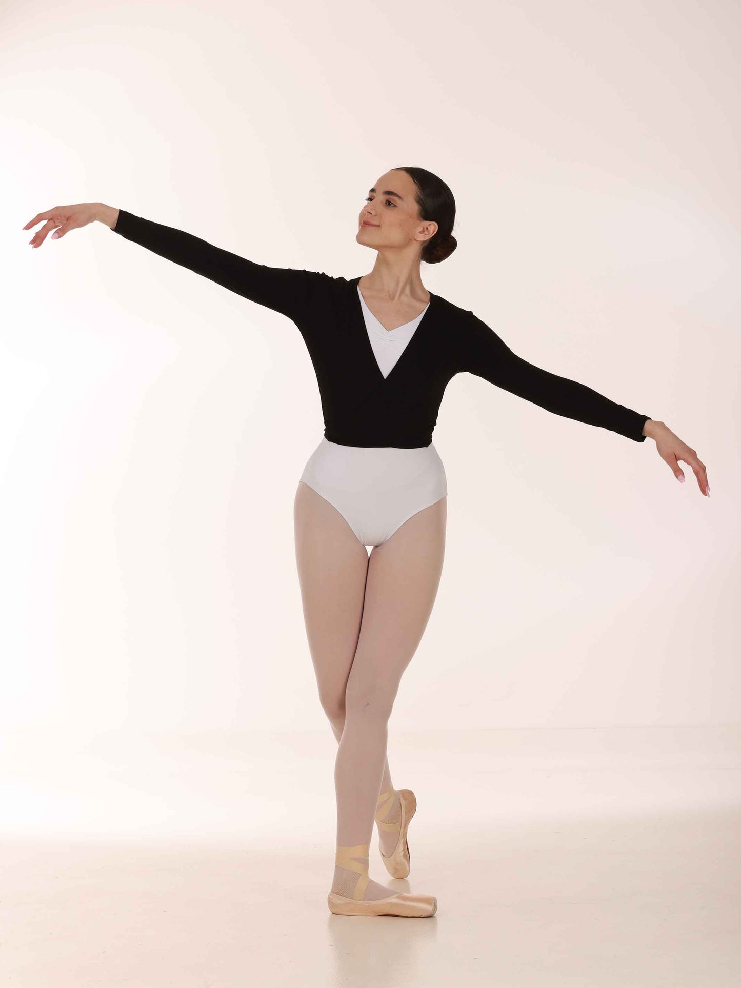 Ballerina in a black long-sleeve warmer crossover and white leotards posing on a light background