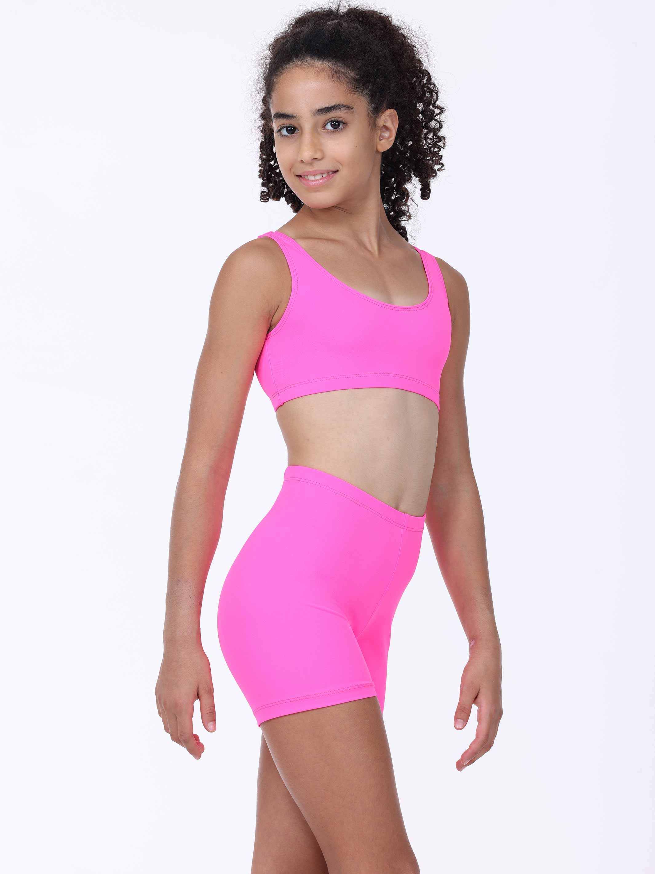 Young girl wearing a bright pink sports bra and shorts set on a white background