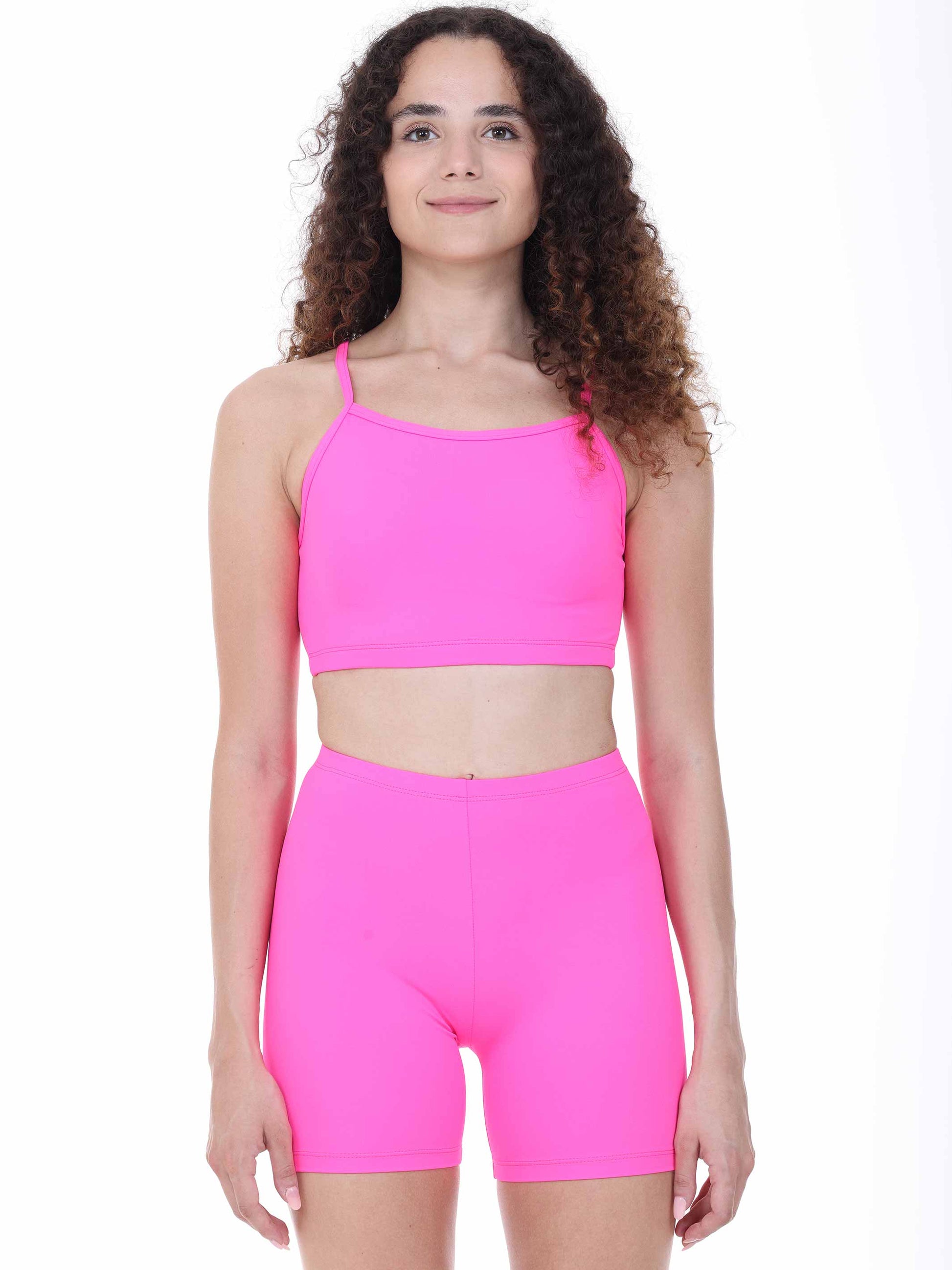 Woman wearing a bright fuchsia sports bra and shorts set on a white background