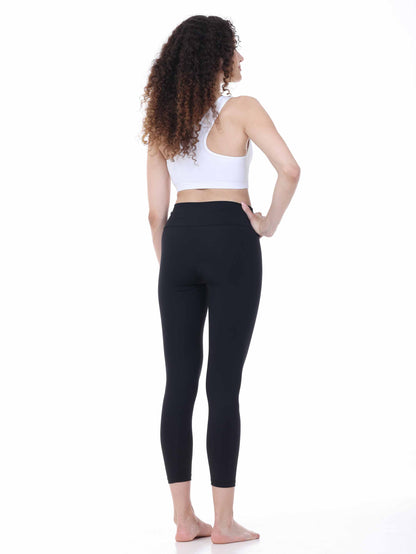 Woman wearing black leggings and a white sports bra on a white background