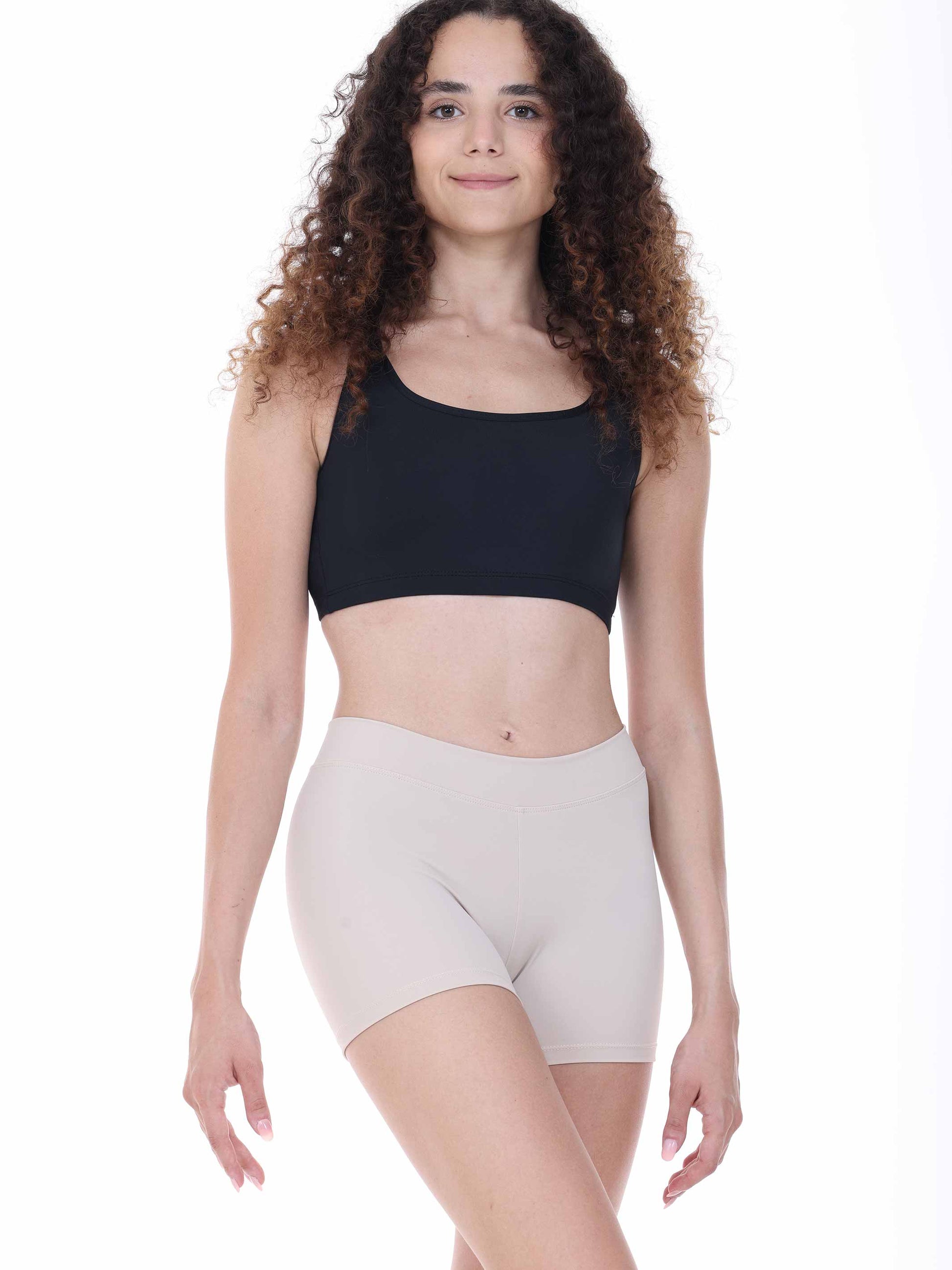 Woman wearing a black sports bra and beige shorts on a white background
