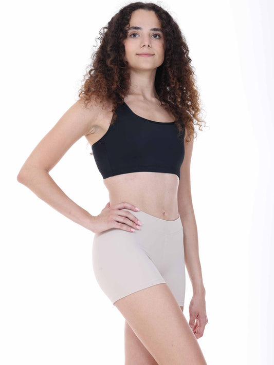 Woman wearing a black sports bra and nude shorts on a white background