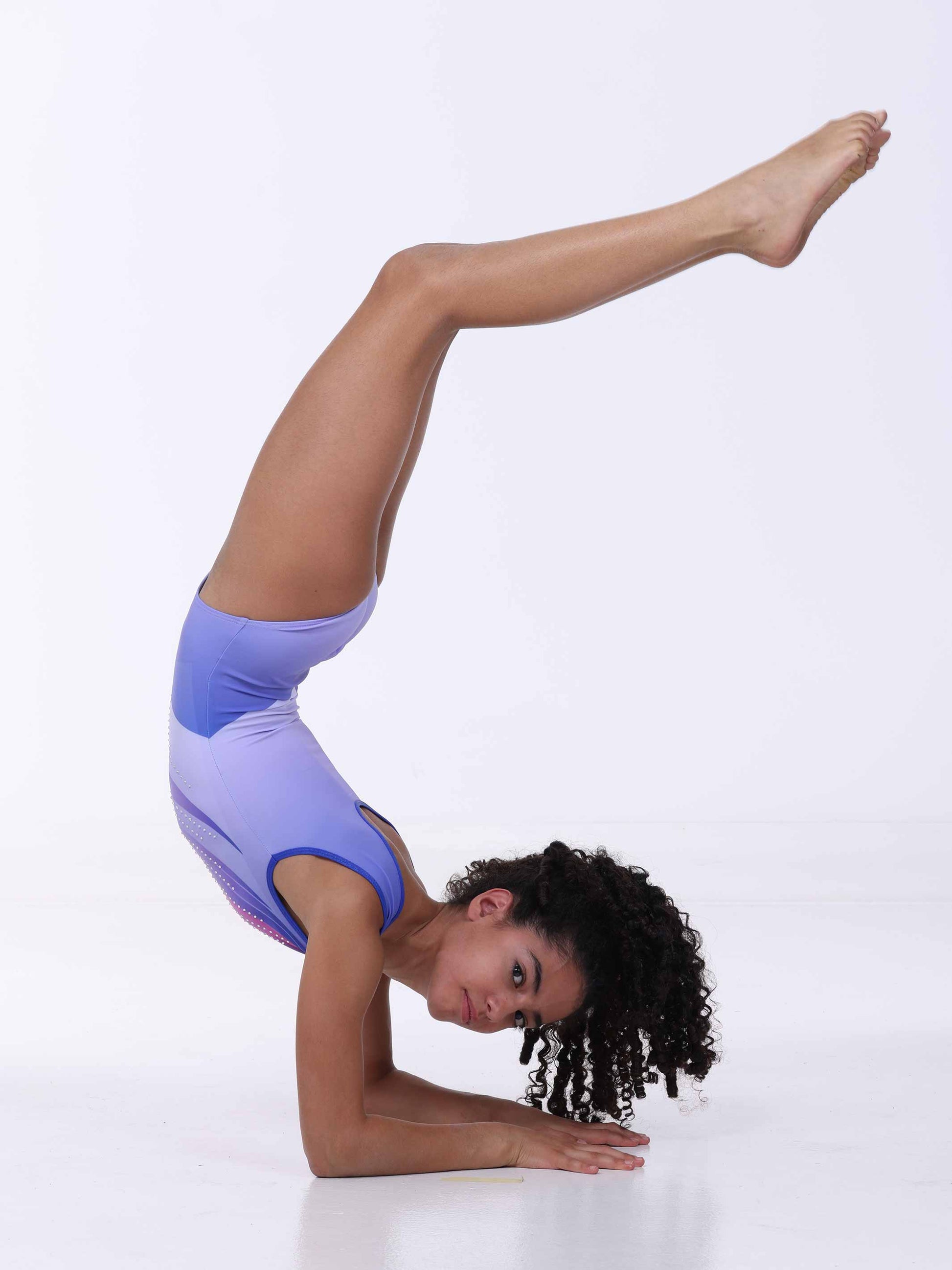 Girl in a gymnastics pose wearing a purple gymnastics outfit on a white background